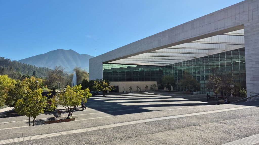 Imagen que retrata la entrada y la fachada principal del Teatro Mori en Vitacura, un espacio cultural muy reconocido. Se aprecia su moderna arquitectura con una gran fachada de vidrio. Un hombre camina hacia la entrada del teatro.